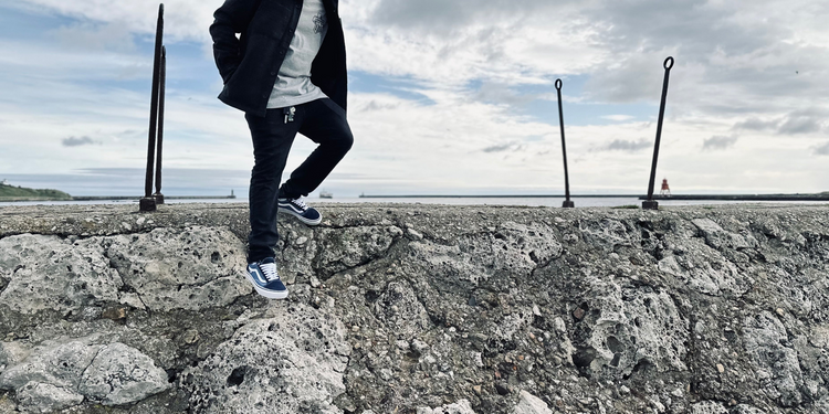 Adam, our Longsands Après bar manager, wearing the adventure jacket "Bold Shacket" in black. He is climbing down some coastal rocks at the Fish Quays in the North East of England